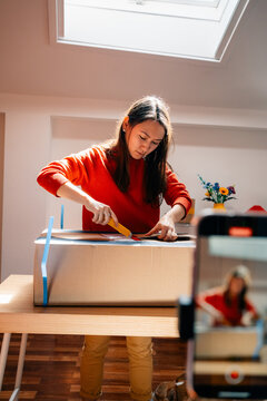 Woman cutting cardboard box in packaging workspace