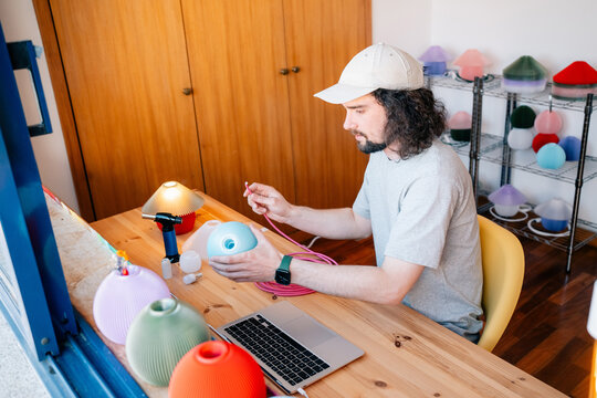 Man assembling colorful lamp with electric cable at desk
