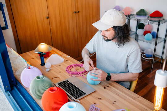 Man assembling colorful lamp with cable at desk