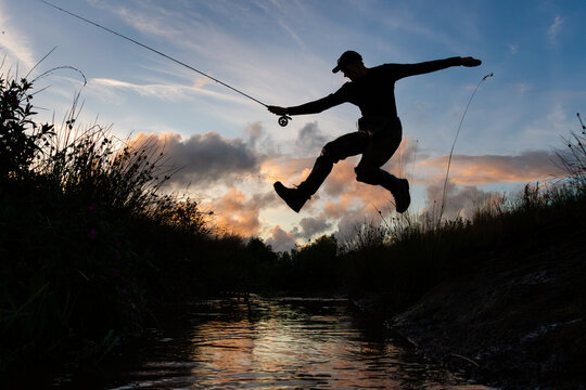 Man leaps over creek with fishing rod in hand
