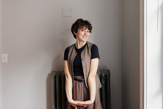 Young woman near apartment window smiles cheekily at camera