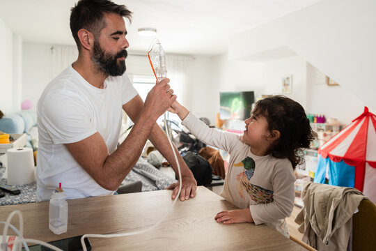 Father using a nebulizer at home with his daughter helping him