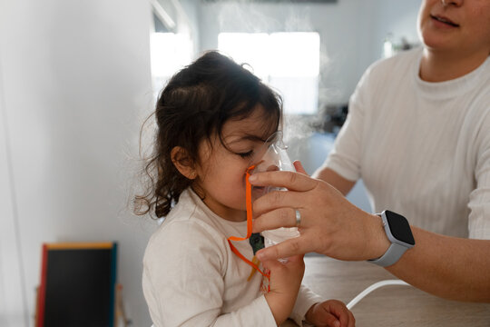 Mother helping her sick daughter inhaling with nebulizer mask