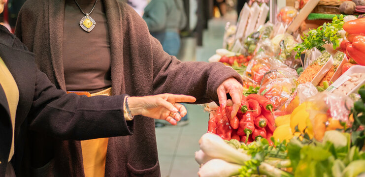 Shoppers' hands choosing red peppers from a vibrant display of produce at an indoor market
