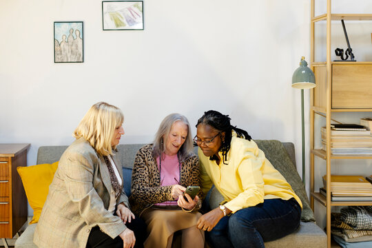 Group of three female friends at home living room checking smartphone