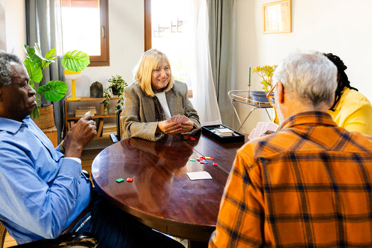 Group of senior friends playing cards at home living room