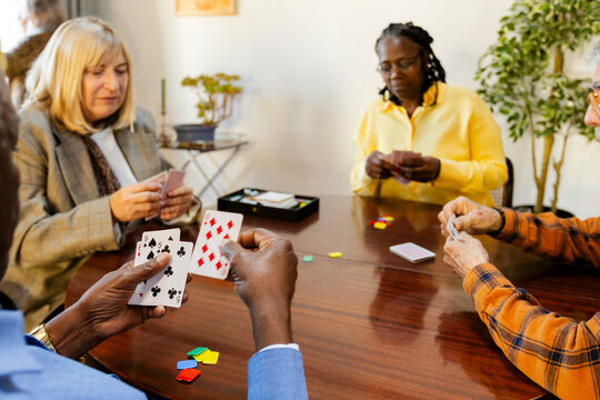 Crop of  senior friends playing cards at home living room