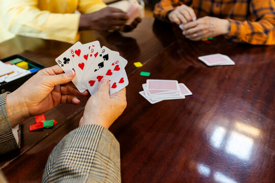Crop of  anonymous senior friends playing cards at home living room