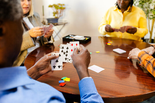 Crop of  senior friends playing cards at home living room