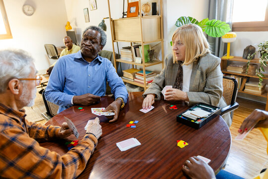 Group of senior friends playing cards at home living room