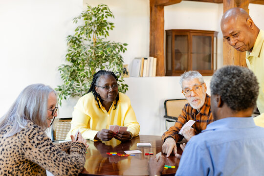 Group of senior friends playing cards at home living room