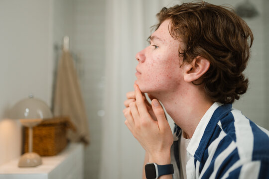 A man examines his face with pimples in the mirror