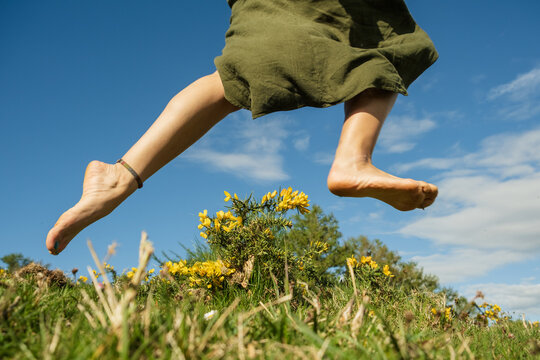 Woman jumping barefoot among yellow flowers