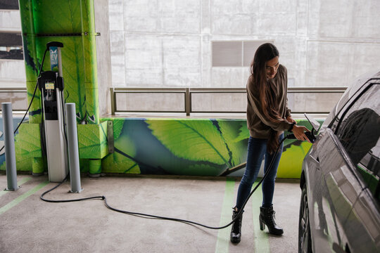 Woman Charging Electric Car at Eco-Friendly Green Parking Facility