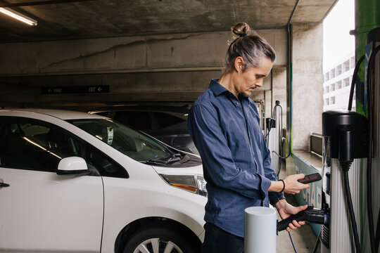Man Charging Electric Car at a Parking Garage with His Smart Device