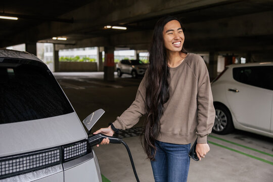 Smiling Woman Charging Electric Car in Parking Garage Environment