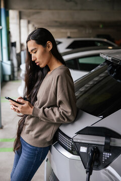 Woman Checking Her Smartphone While Charging Electric Vehicle