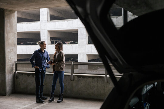 Two People Interacting in a Parking Garage Near an Open Car Trunk