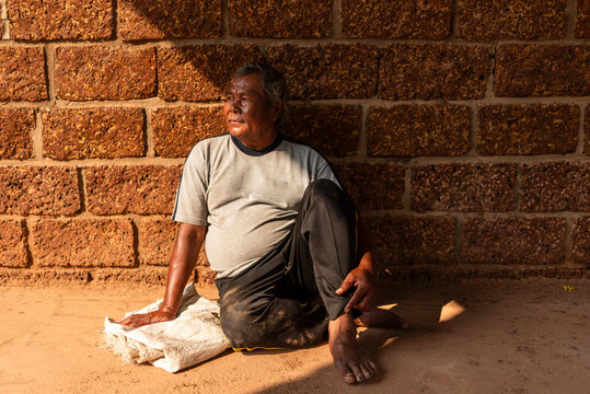 Elderly Thai man resting against temple wall on a hot day