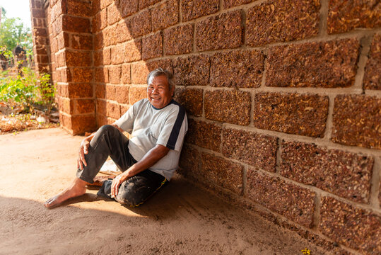Elderly Thai man resting by temple wall with a smile in urban Thailand