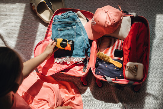 Girl's hand puts down camera at pink suitcase for travelling.