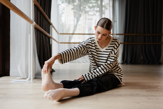 Dance student stretching legs on floor in dance studio