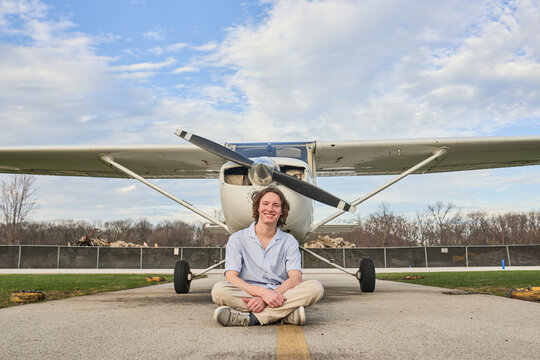 Smiling teen sitting in front of a small propeller airplane