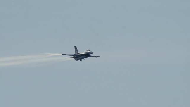 MADRID, SPAIN - OCTOBER 12, 2025: Video of a powerful F-16 fighter jet performing a high-G acrobatic maneuver. The aircraft banks sharply, leaving dramatic white vapor trails across the clear blue sky