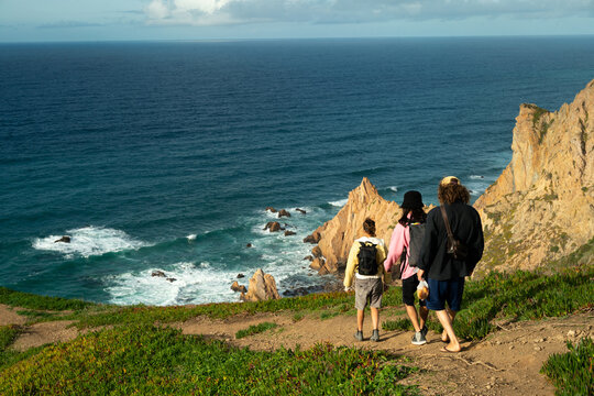 Three people walking down hiking trail by cliff beach