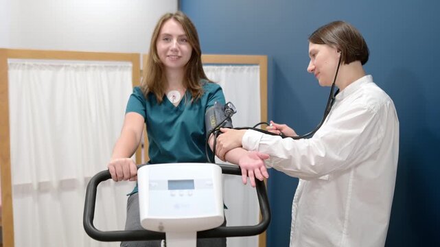 Female doctor cardiologist measures pressure with patient during bicycle exercise for examination cardiovascular system at medical clinic. Young woman training on bike simulator. Exercise bike