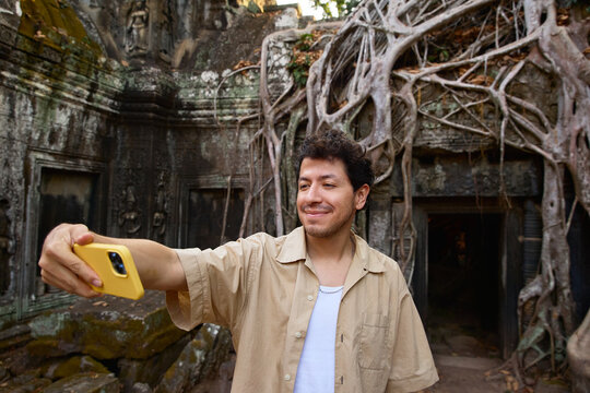  Man taking selfie by tree-covered temple Ta Prohm in Cambodia