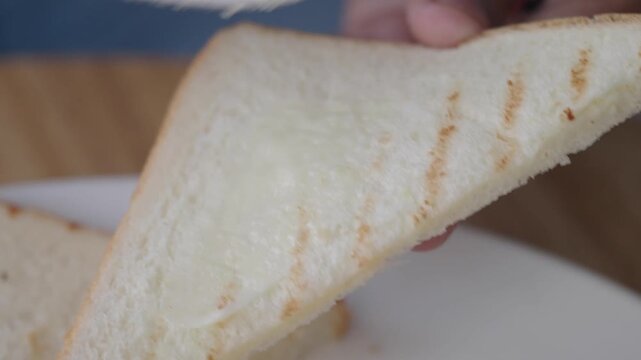 Close-up cinematic motion footage of person spreading butter on a piece of toasted white bread with a knife in slow motion