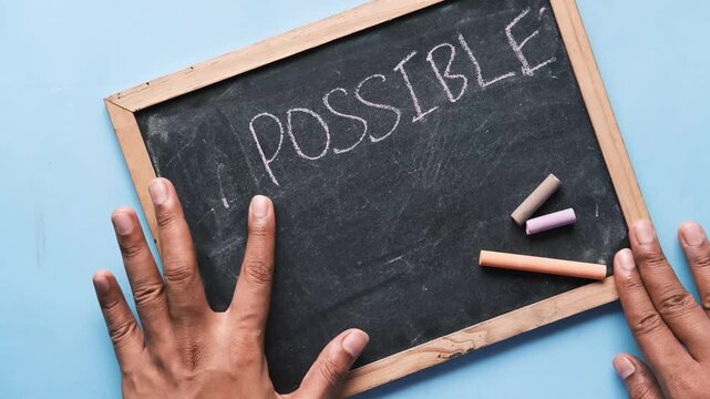 Person erasing letters on chalkboard to change word impossible to possible