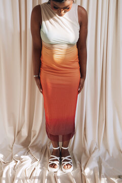 Woman in gradient dress looking down against curtain backdrop