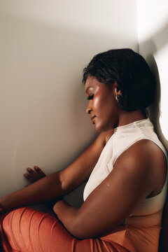 Sad woman sit against sunlit wall