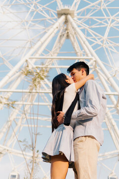 Couple kissing infron of ferris wheel.