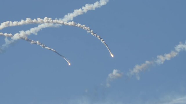 MADRID, SPAIN - OCTOBER 12, 2025: Multiple military aircraft countermeasures, bright burning flares, are released against a clear blue sky. They leave long, arcing trails of white smoke as a decoy for