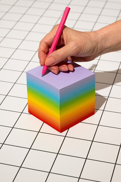Hand holding a pen writing on a rainbow colored notepad