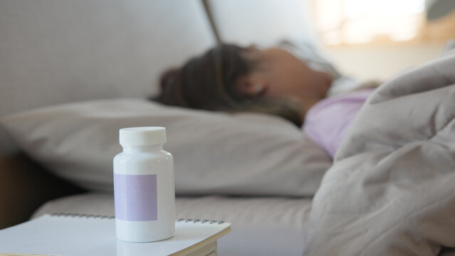 Young adult woman black asia people take herbal CBD pill bottle lying down on soft cozy bed deep sleep aid calm. Waking up happy serene relax drug anti aging good health care fall asleep till morning.
