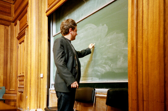Man Writing on Chalkboard in Lecture Hall