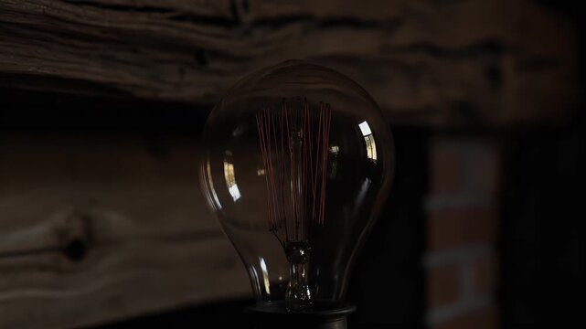 Close-up of an illuminated Edison bulb with visible filament against a dark, rustic background