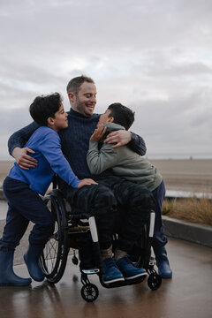 Father In Wheelchair Embracing His Children by the Beach