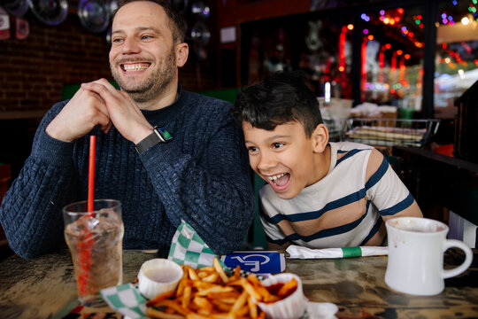 Father and Son Laughing Together Over Meal in a Cozy Restaurant