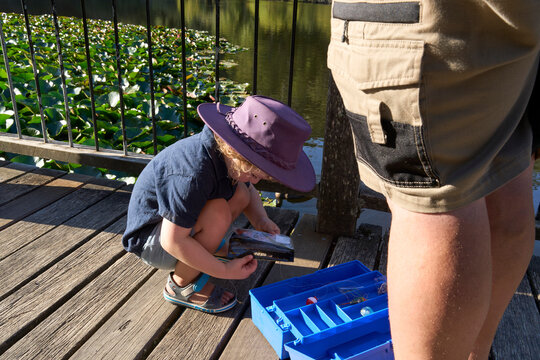 Child on Wooden Dock with Tackle Box and Calm Water in Background