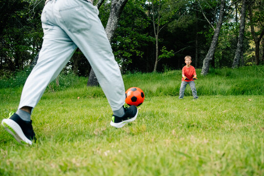 Person kicking soccer ball toward child on green field