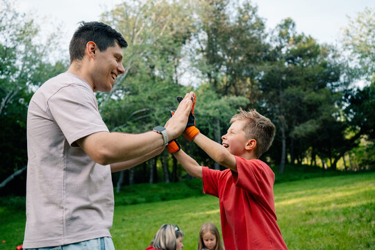 Child and adult sharing high five in grassy park with trees