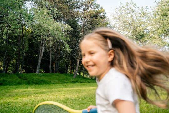 Smiling child with racket running through grassy park
