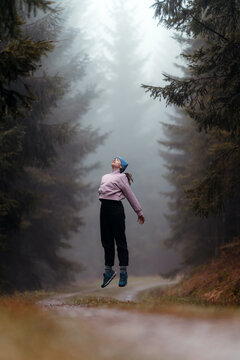 Woman jumping and levitating in a winter forest with fog