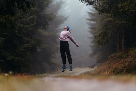Woman jumping and levitating in a winter forest with fog