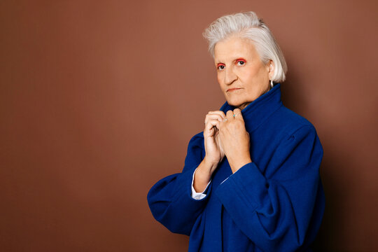 Stylish senior woman pulling up collar of blue coat on